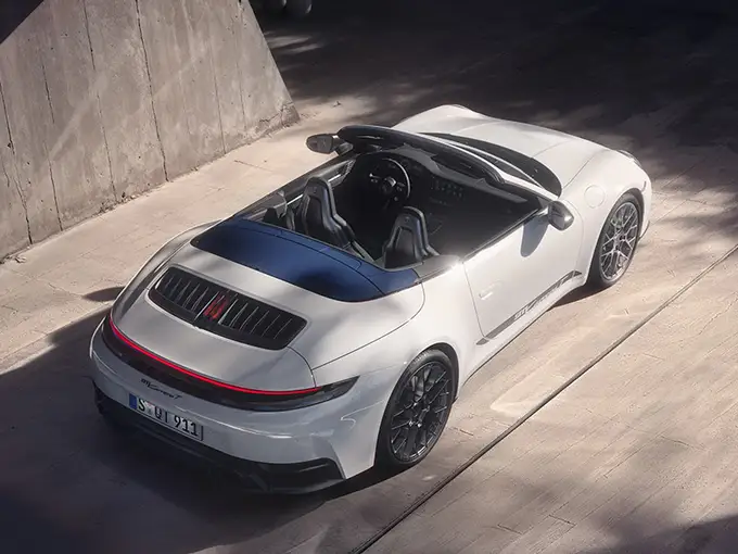 White 911 Carrera T sports car parked on a sunlit concrete surface, viewed from above, with sleek design and black interior.